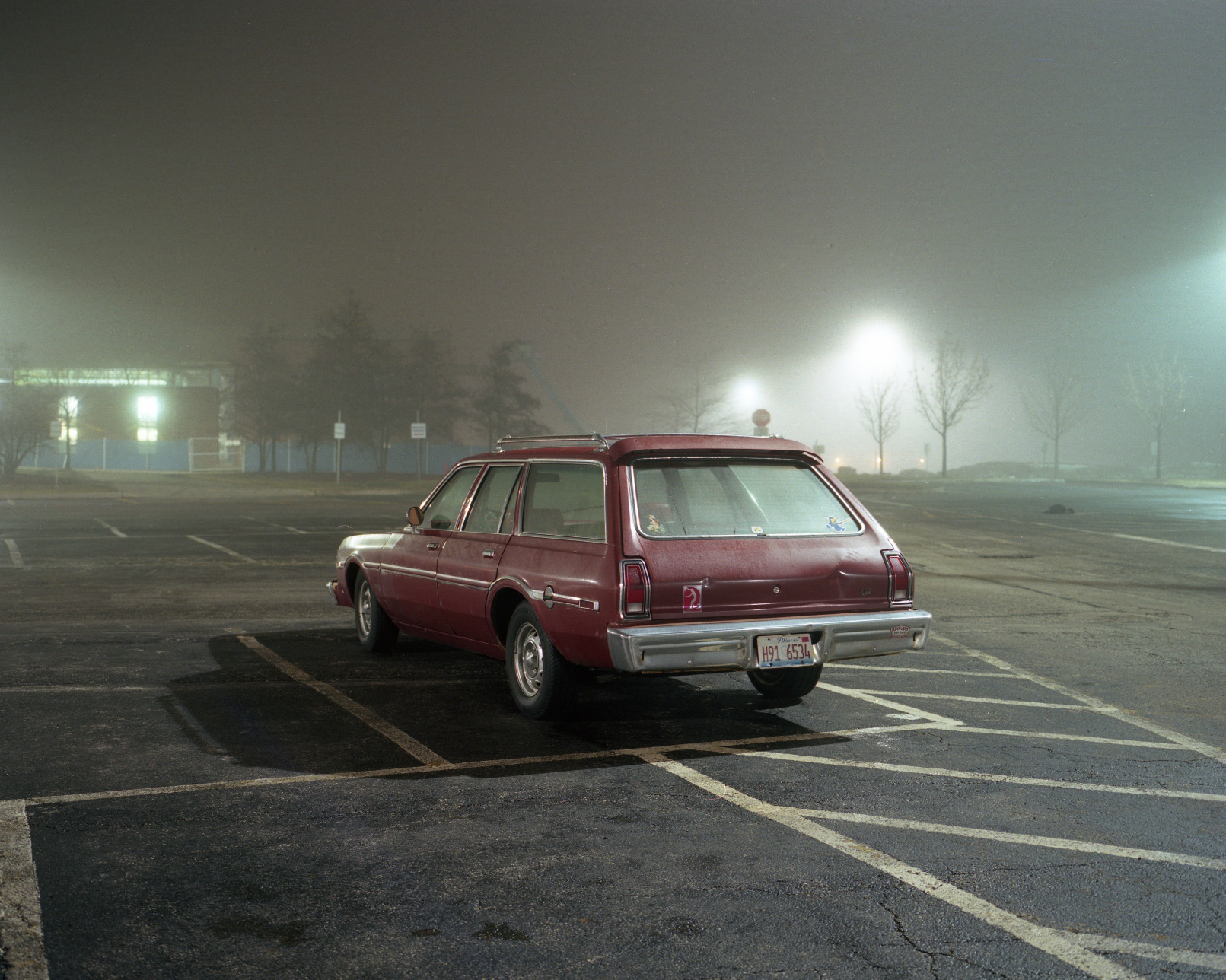 Red car in a parking lot during a foggy night