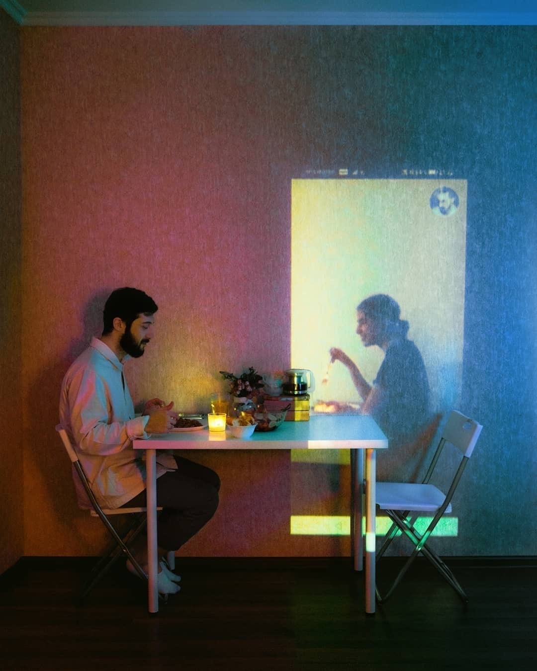 Man eating dinner, with woman being beamed on a wall taken from a smartphone conversation 