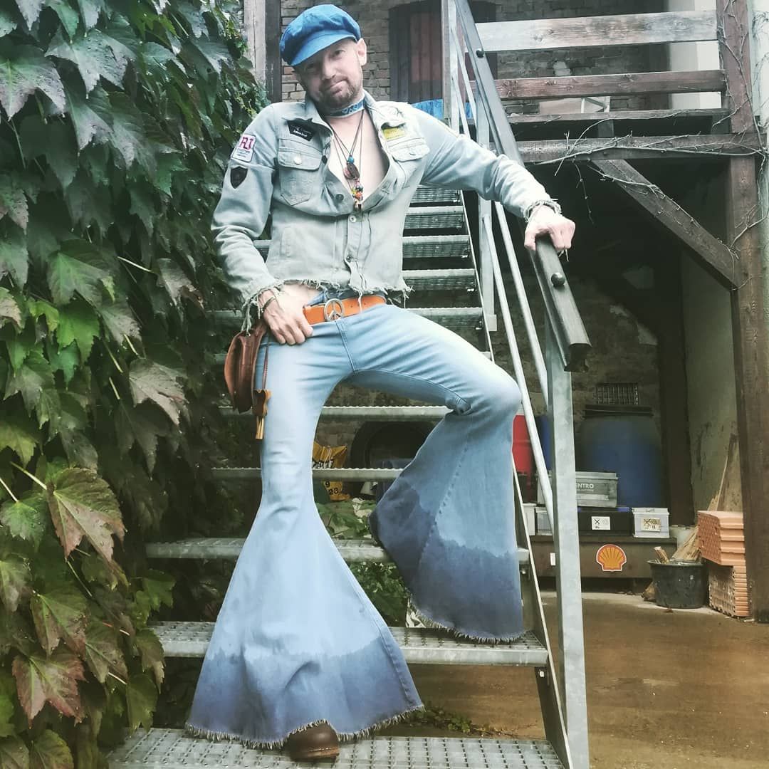 A guy in comically big bell bottom jeans. He is standing on stairs and poses with the jeans.