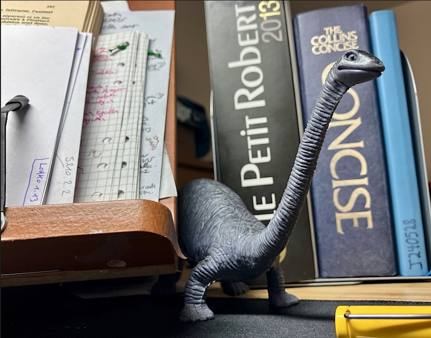 a photo of the toy dinosaur that lives on my home desk, between books and notes, mostly feeding on scrap paper