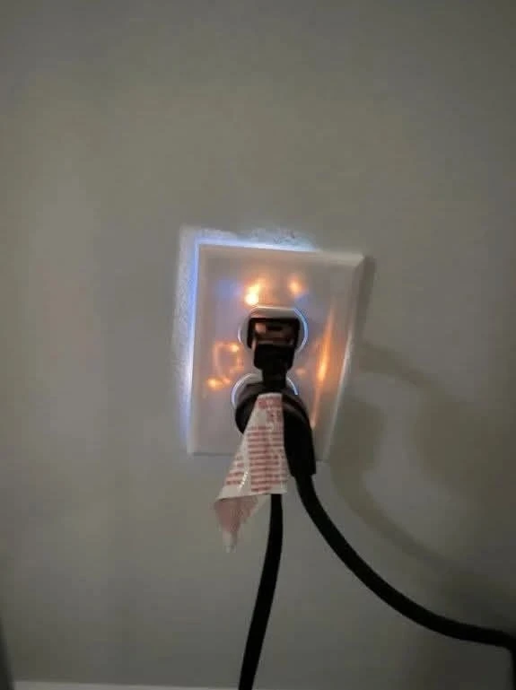 photo of an electrical socket, behind the plastic cover the wires glow bright orange. blue flashes escape from the edges of the cover