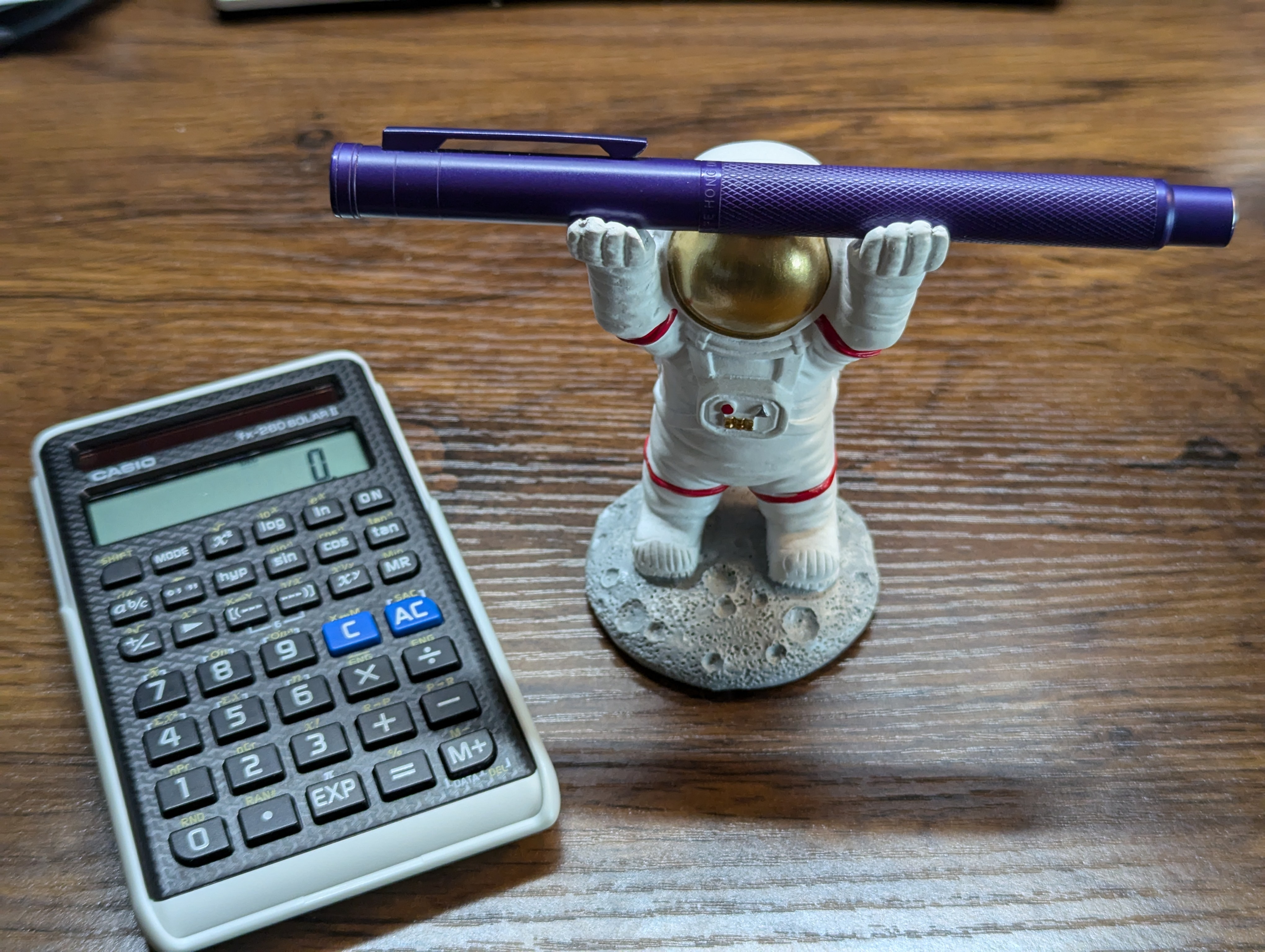 Hongdian 1851 Forest Purple fountain pen held aloft by a pen holder shaped like an astronaut.  A Casio fx-260 Solar II calculator is next to it.